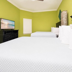 This guest bedroom features two comfortable queen beds, a vibrant green accent wall with fun decor, and a TV and dresser