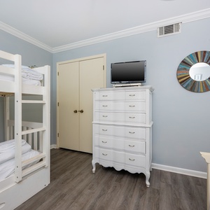 This cozy bedroom features a white bunk bed, a TV for entertainment, and a charming dresser with a colorful mirror