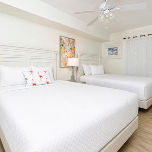 This guest bedroom featuring two queen beds with white bedding, a colorful flamingo pillow, and cheerful artwork on the walls