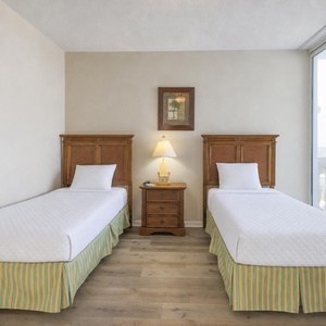 This bedroom features two twin beds with colorful striped skirts, a bedside lamp, and large windows offering a beautiful view