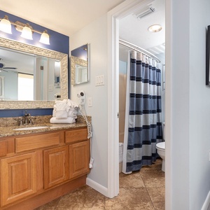 The master bath features a wooden vanity with a large mirror, neatly stacked towels, and a shower with a striped curtain