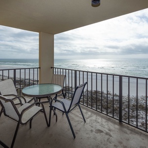 Balcony featuring a glass-top table and chairs, offering a serene view of the shimmering water and white sand below