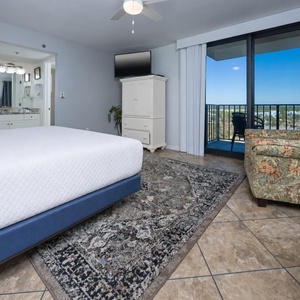 Relaxing master bedroom featuring a king bed, floral armchair, and a balcony with a scenic view