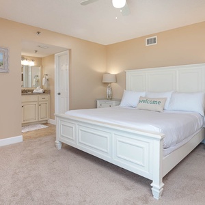 A serene master bedroom features a king bed with plush linens, a decorative pillow, and a view of the adjoining bathroom