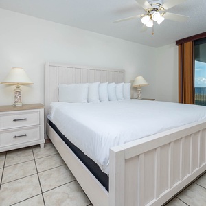 Bright and airy master bedroom featuring a king bed, coastal decor, and direct access to the balcony with a view of the beach