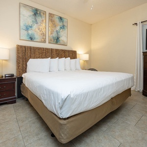 Cozy bedroom featuring a large king bed with decorative pillows, a wooden dresser, and a flat-screen TV
