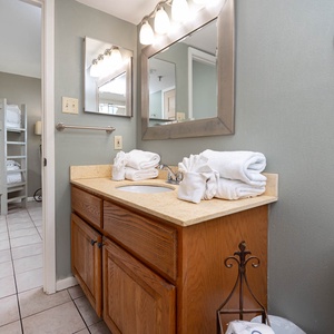 The bathroom features a wooden vanity with a sink, neatly stacked towels, and a tub/shower combo for a refreshing stay