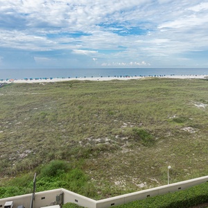 Expansive view of the beach with vibrant umbrellas lining the shore, framed by lush greenery and gentle waves in the distance