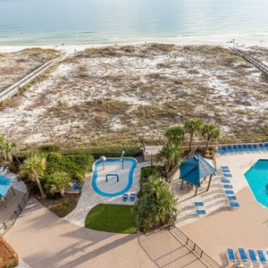 Inviting pool and splash park area surrounded by palm trees and lounge chairs, just steps from the beach access