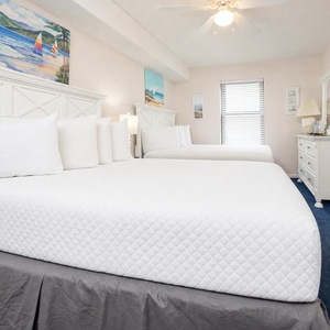 Bright guest bedroom featuring two double beds, soft linens, and coastal artwork, creating a relaxed vacation atmosphere