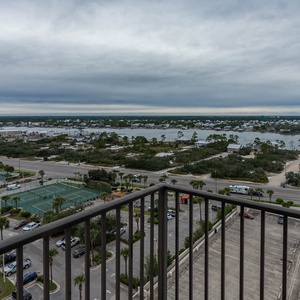 The master balcony view showcases lush greenery, tennis courts, and the tranquil waters of the nearby bay
