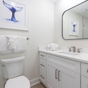 This bathroom features a vanity with sleek fixtures, fluffy towels, and a serene whale art piece for a refreshing touch