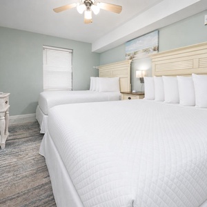 Two comfortable queen beds with crisp white linens and a mounted TV create a serene atmosphere in this inviting guest room