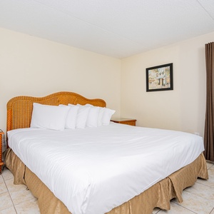 The bedroom features a cozy bed with decorative pillows and a lovely view of the beachfront through large windows