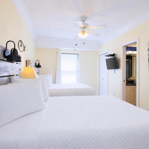 Cozy guest room featuring two double beds, a mounted TV, and easy access to the bathroom with fresh towels