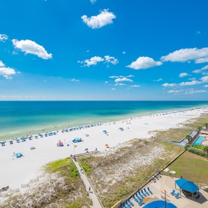 Enjoy a panoramic view of the beach with white sand and colorful umbrellas stretching along the tranquil shoreline