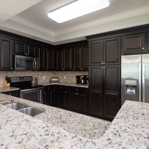 Prepare meals in this stylish kitchen featuring dark cabinetry, granite countertops, and stainless appliances