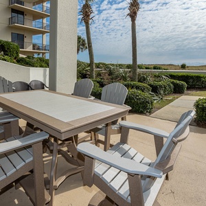 Outdoor dining area features a large table surrounded by comfortable chairs, with lush greenery and palm trees in view