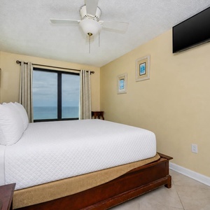 This bedroom features a king-size bed, a wall-mounted TV, and a stunning beachfront view through large windows