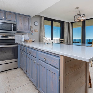 Bright kitchen features blue cabinetry, stainless appliances, Keurig, coffee maker, and a view of the beach