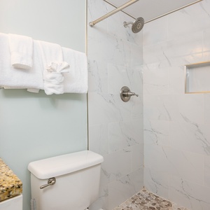 Modern master bathroom featuring a sleek walk-in shower, elegant granite countertop, and fluffy white towels