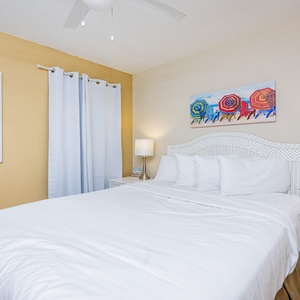Inviting guest bedroom featuring a cozy queen bed, colorful beach umbrella artwork, and soft natural light
