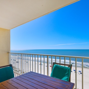 Enjoy a stunning beachfront view from the private balcony, featuring a wooden table and comfortable seating