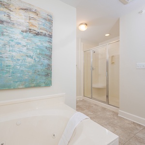 Relax in this serene master bathroom featuring a jetted tub, modern walk-in shower, and calming coastal artwork