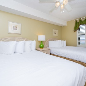 Guest bedroom featuring two queen beds with plush white linens, a green lamp, and a window dressed with colorful curtains
