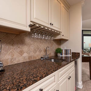 This stylish wet bar features elegant cabinetry, a granite countertop, and a cozy seating area just beyond