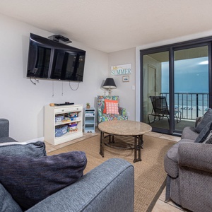 This cozy living area features a large TV, comfortable seating, and a vibrant view of the beach from the balcony