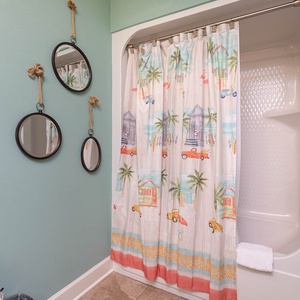 This bathroom features playful beach-themed decor, including vibrant shower curtains and stylish mirrors