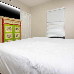 Rest in this guest room featuring a comfortable king bed, a colorful dresser, and a mounted TV for your entertainment
