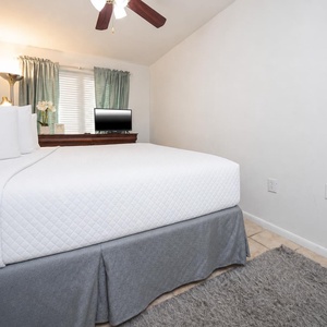 This bedroom features a comfortable bed, a TV for entertainment, and soft green curtains for a relaxing atmosphere
