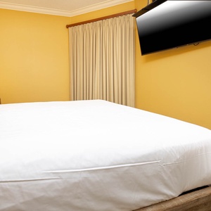 Experience restful nights in this guest bedroom with a plush queen bed, warm yellow walls, and a mounted TV for entertainment