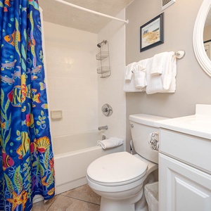 This guest bath features a colorful fish-themed shower curtain, fresh towels, and a clean, bright atmosphere