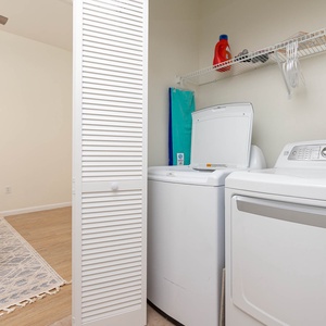 Laundry area featuring a washer and dryer, with a shelf above for storage and a glimpse of the adjoining guest bedroom