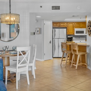 The dining area features a round wooden table set for four, complemented by a breakfast bar and a view into the kitchen