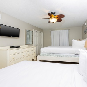 Charming guest bedroom featuring two double beds, a wall-mounted TV, and a dresser, perfect for relaxing after beach days
