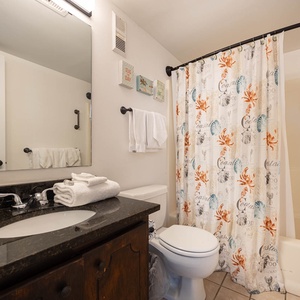 This bathroom features a stylish dark countertop, vibrant coastal-themed decor, and fresh towels for a welcoming touch