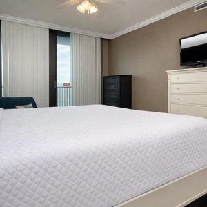 Spacious master bedroom featuring a king bed, flat-screen TV, and large windows with a view of the balcony