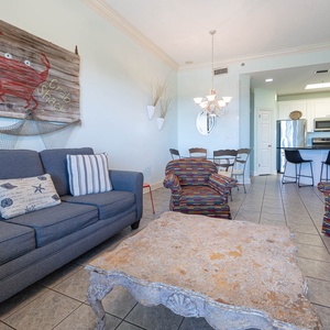 Cozy living area features a blue sofa with striped pillows, colorful accent chairs, and a rustic coffee table