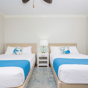Rest in the guest room featuring two queen beds adorned with beach-themed decor and a nightstand lamp