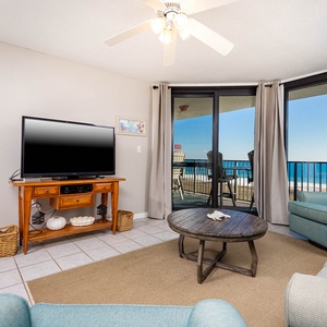 Cozy living area features a TV, comfortable seating, and sliding glass doors opening to a balcony with a view of the gulf