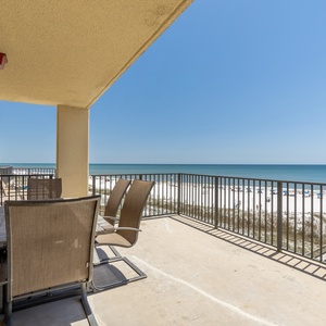 Extended balcony features a dining table and chairs, offering a serene view of the beach and tranquil waters beyond