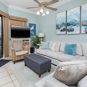 Cozy living area features a light gray sofa with decorative pillows, a woven chair, and vibrant beach artwork