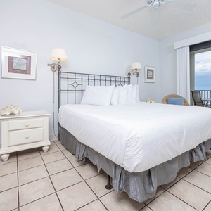 Bright master suite featuring a king bed, coastal decor, and access to a balcony with views of the tranquil gulf