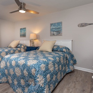 Charming guest bedroom featuring two double beds, coastal decor, and a ceiling fan for added comfort