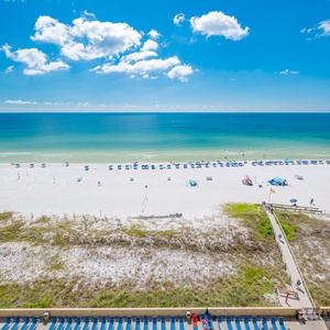 The vibrant beach stretches below, dotted with colorful umbrellas and lounge chairs against a backdrop of turquoise waters