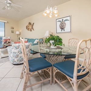A glass dining table with bamboo chairs complements the coastal decor, while large windows showcase a serene beach view